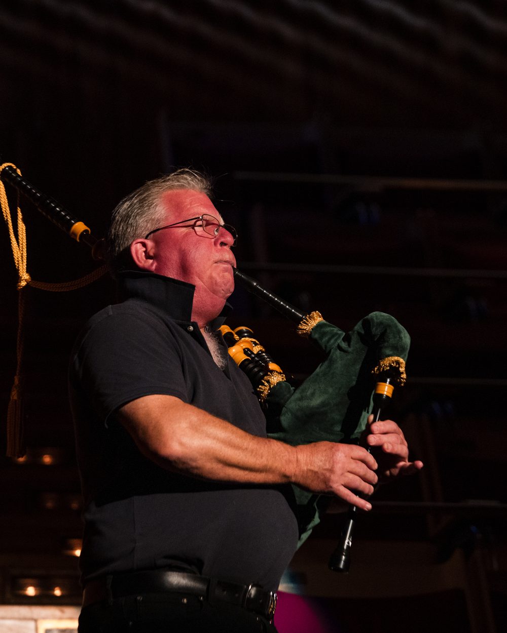 A lone piper playing in a single spotlight on a dark concert hall stage