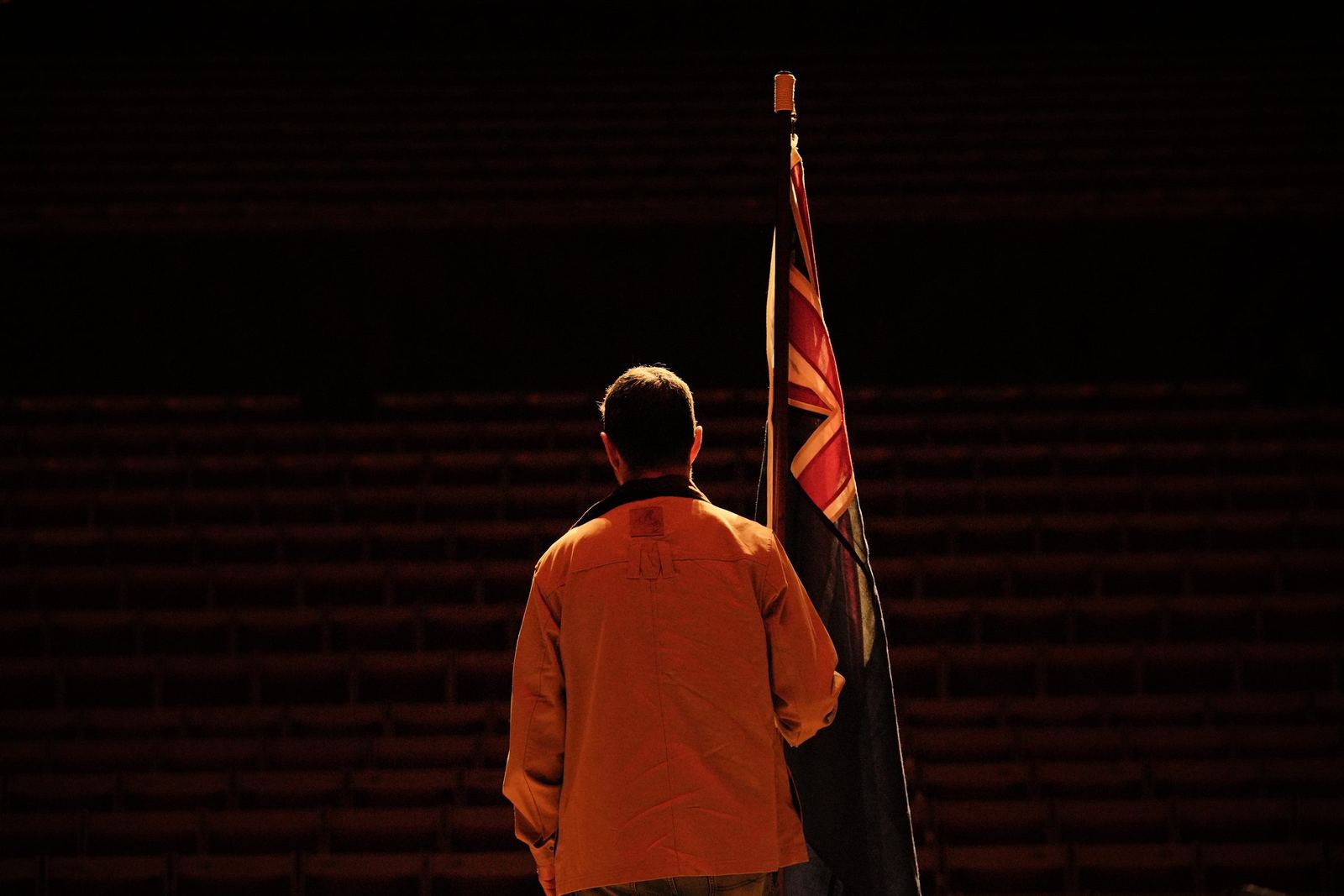 A lone figure beside the flag in the darkened hall